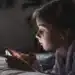 "Menina pequena usando um smartphone na cama, focada na tela, representando a questão do uso de dispositivos por crianças.