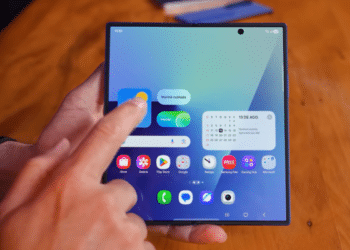 Mão interage com smartphone dobrável exibindo tela inicial e widgets