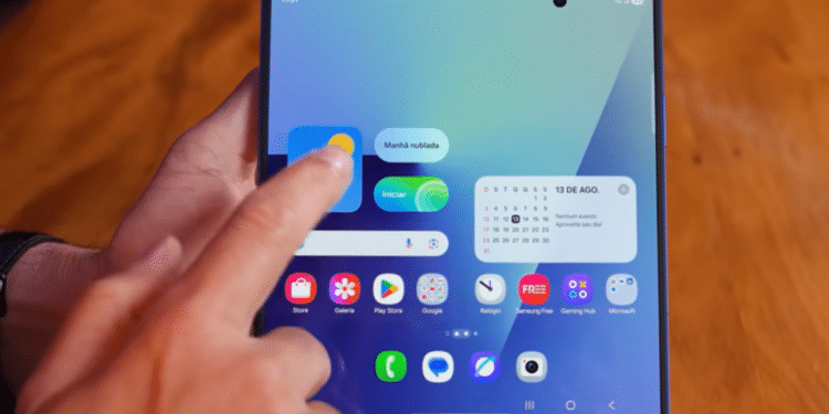 Mão interage com smartphone dobrável exibindo tela inicial e widgets