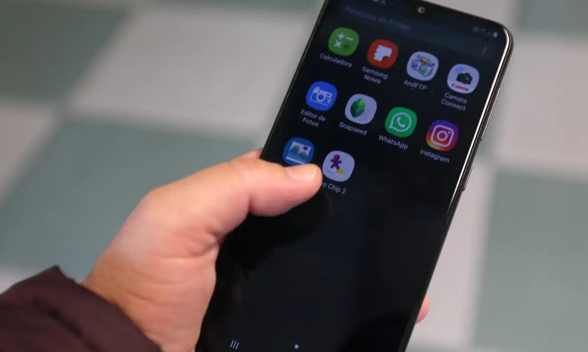 Pessoa segura smartphone exibindo tela com ícones de WhatsApp, Instagram e outros apps