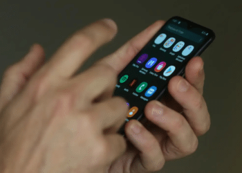 Mãos utilizando smartphone com aplicativos abertos na tela iluminada
