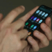 Mãos utilizando smartphone com aplicativos abertos na tela iluminada