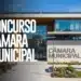 Prédio da Câmara Municipal com fachada de vidro e letreiro, jardim em destaque