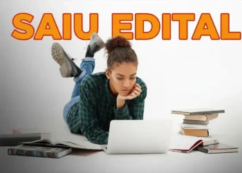 Mulher concentrada em seu laptop, cercada por livros, lendo sobre o concurso público da prefeitura com salários de até R$ 12 mil e inscrições abertas em 27/03.