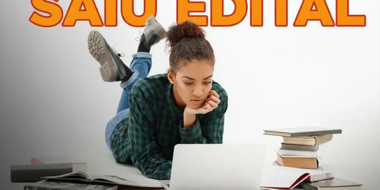 Mulher concentrada em seu laptop, cercada por livros, lendo sobre o concurso público da prefeitura com salários de até R$ 12 mil e inscrições abertas em 27/03.