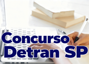 Mão digitando em notebook ao lado de caderno e caneta sobre mesa branca