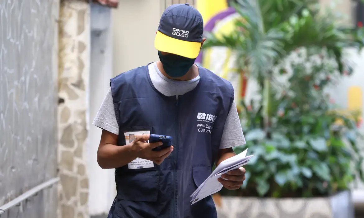 Recenseador do IBGE com uniforme e boné, trabalhando nas ruas, em meio ao processo do Censo 2020.