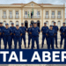 Grupo de guardas municipais uniformizados alinhados em praça diante de prédio histórico