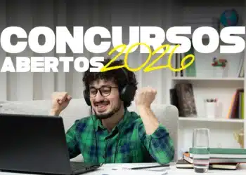 Homem sorrindo com fones de ouvido, vibrando em frente ao notebook, rodeado de livros
