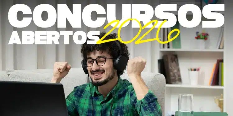 Homem sorrindo com fones de ouvido, vibrando em frente ao notebook, rodeado de livros