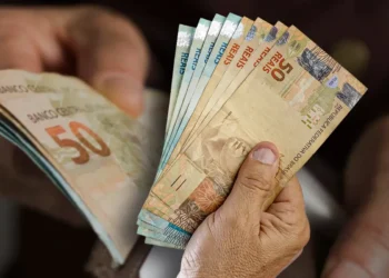 Notas de 50 reais em mãos representando o pagamento do 13º salário do INSS aos beneficiários.