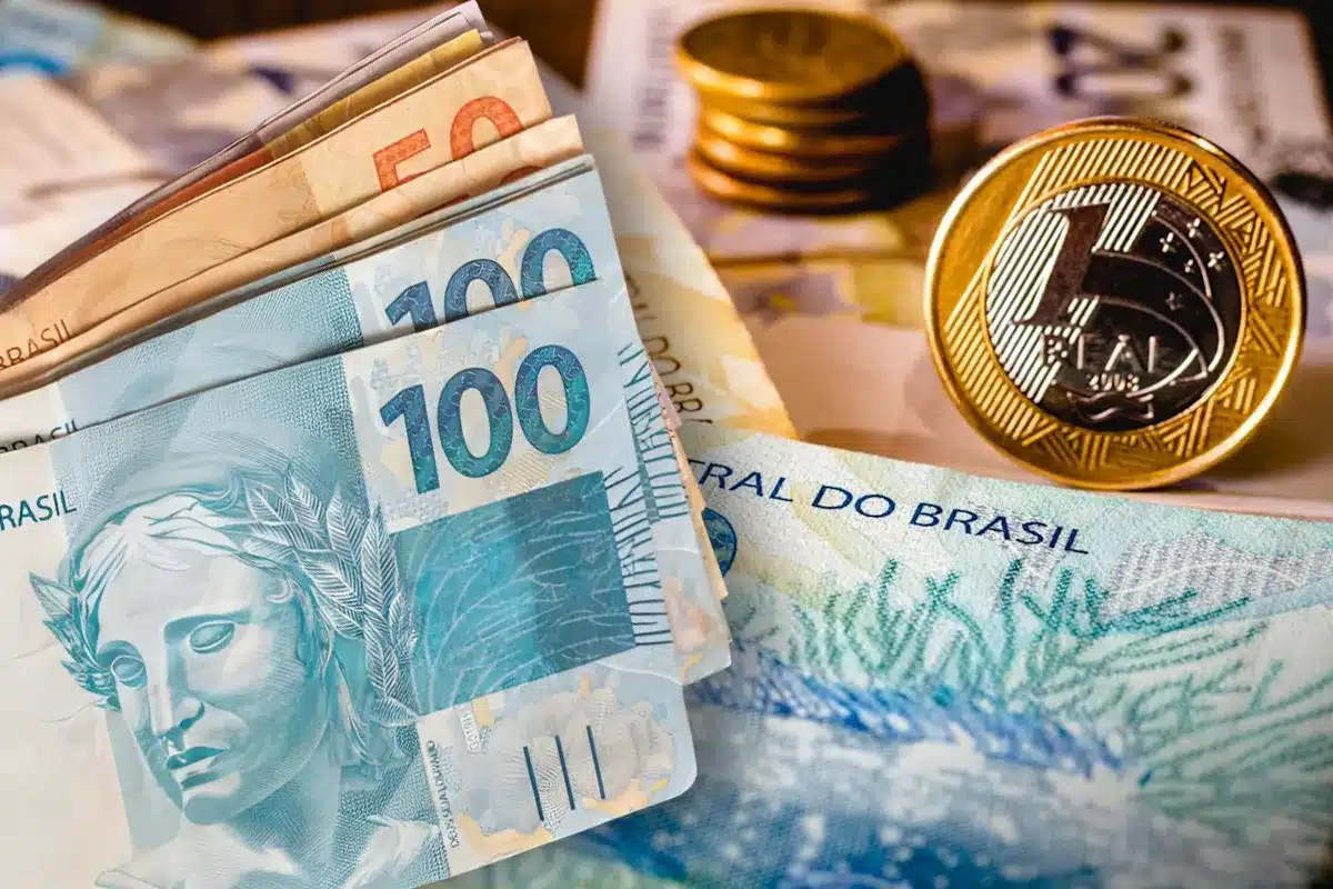 Cédulas e moedas do real, incluindo notas de R$ 100 e R$ 50, representando o depósito do Pé-de-Meia.