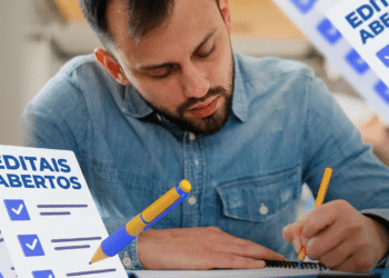 Jovem escreve em caderno enquanto segurando caneta, ao lado de cartaz com "Editais Abertos"