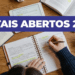 Pessoa escrevendo em caderno ao lado de livros, tablet e café em mesa de madeira