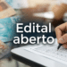 Mão preenchendo cartão de respostas ao lado de notas de R$100 e R$50