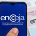 Mão segura celular mostrando logo do Encceja com papéis e caneta ao fundo