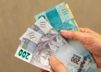 Pessoa segura cédulas de real representando o pagamento dos benefícios do INSS conforme o calendário de agosto de 2026.