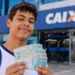Estudante segura cédulas em frente a uma agência da Caixa, representando os pagamentos de agosto do Pé-de-Meia, encerrados nesta segunda-feira, 31.