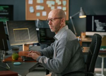 Profissional de tecnologia desenvolvendo comandos para inteligência artificial em ambiente corporativo com múltiplos monitores.