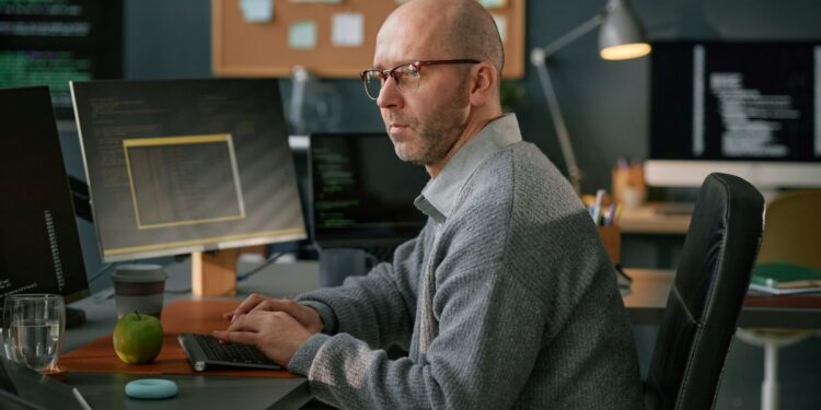 Profissional de tecnologia desenvolvendo comandos para inteligência artificial em ambiente corporativo com múltiplos monitores.