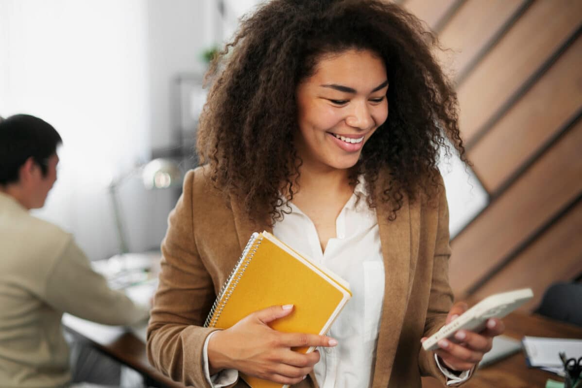 Jovem universitária sorrindo com cadernos e celular no ambiente de trabalho — programa de estágio Bradesco 2026