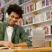 Jovem sorrindo enquanto estuda para concursos públicos, usando fones de ouvido em uma biblioteca.