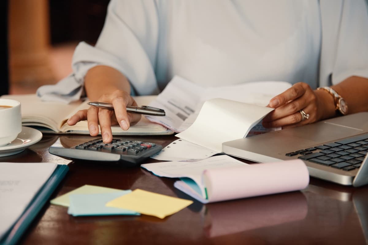 Mulher calculando débitos com calculadora e documentos fiscais representando riscos da exclusão do Simples Nacional