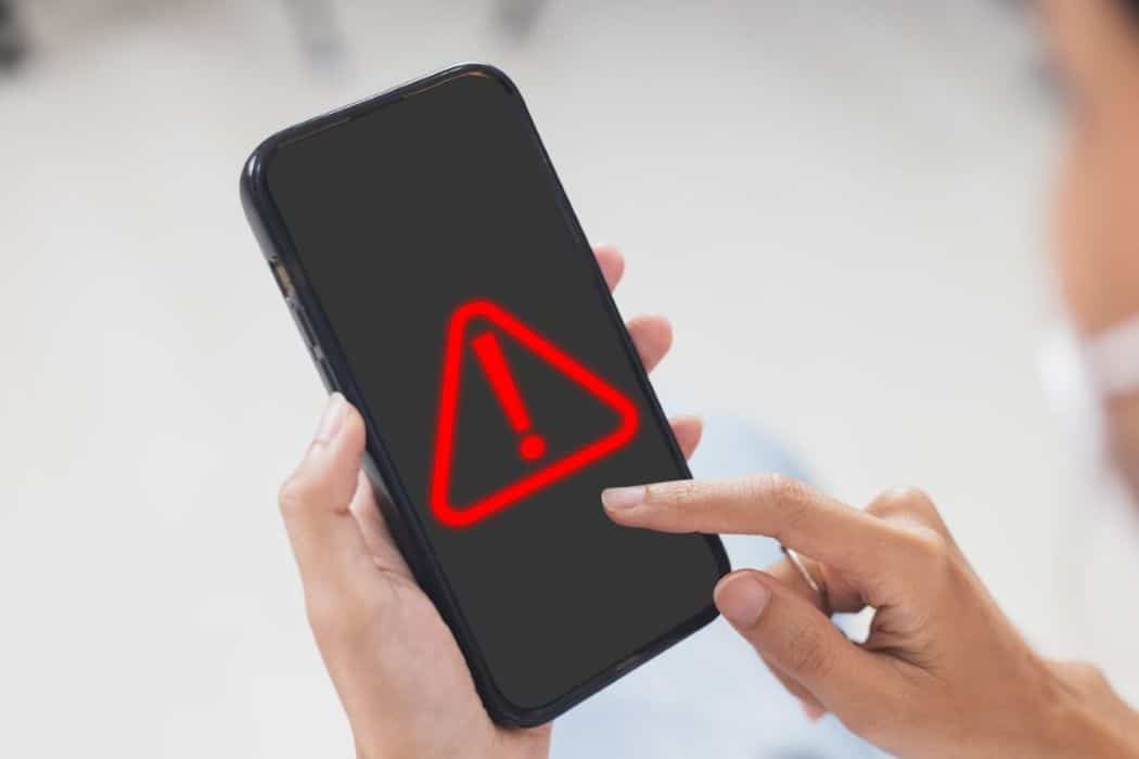 Pessoa utilizando smartphone com alerta de erro, simbolizando os riscos de segurança digital em iPhones.