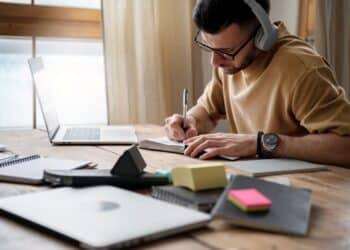 Homem estudando em casa com notebook e caderno enquanto se prepara para decisões de carreira entre faculdade e concursos públicos.