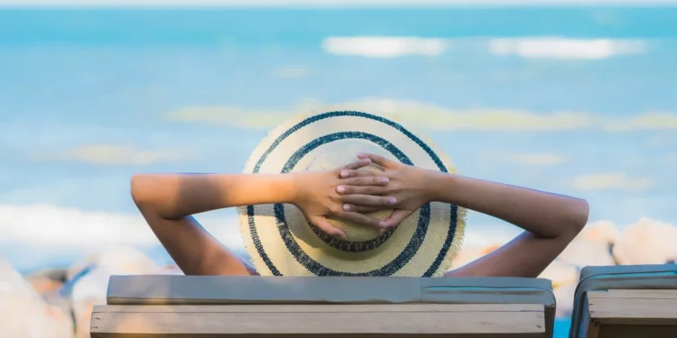 Pessoa relaxando em cadeira de praia observando o mar, representando o planejamento de viagens nos feriados de abril de 2026.