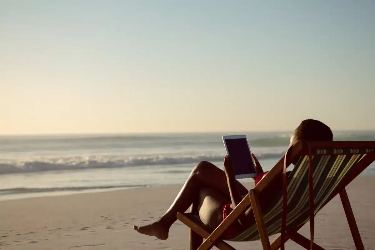 Pessoa relaxando em uma cadeira de praia enquanto consulta um tablet durante um período de descanso em abril