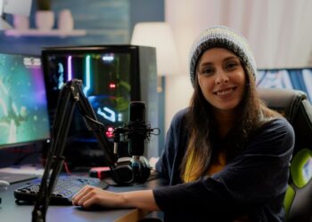 Mulher streamer jogando jogo de tiro espacial em seu computador com teclados RGB e ambiente de estúdio.