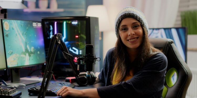 Mulher streamer jogando jogo de tiro espacial em seu computador com teclados RGB e ambiente de estúdio.