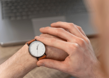 Pessoa ajustando relógio de pulso com pulseira marrom em frente a notebook