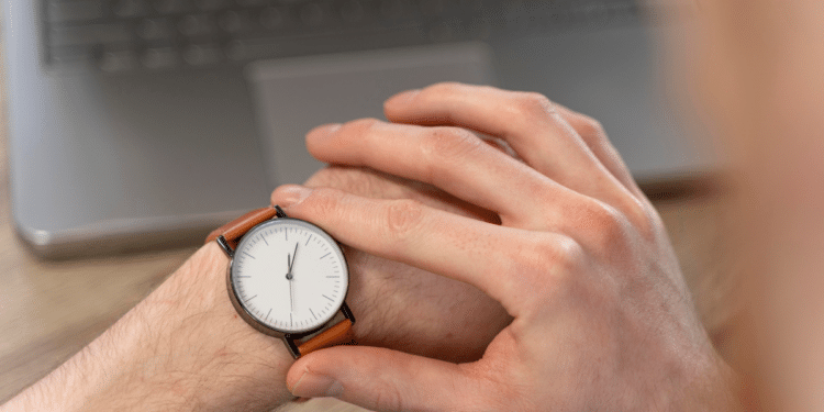 Pessoa ajustando relógio de pulso com pulseira marrom em frente a notebook