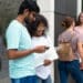 Dois jovens universitários consultando smartphone com notebook em frente a edifício moderno e outras duas estudantes ao fundo em área externa