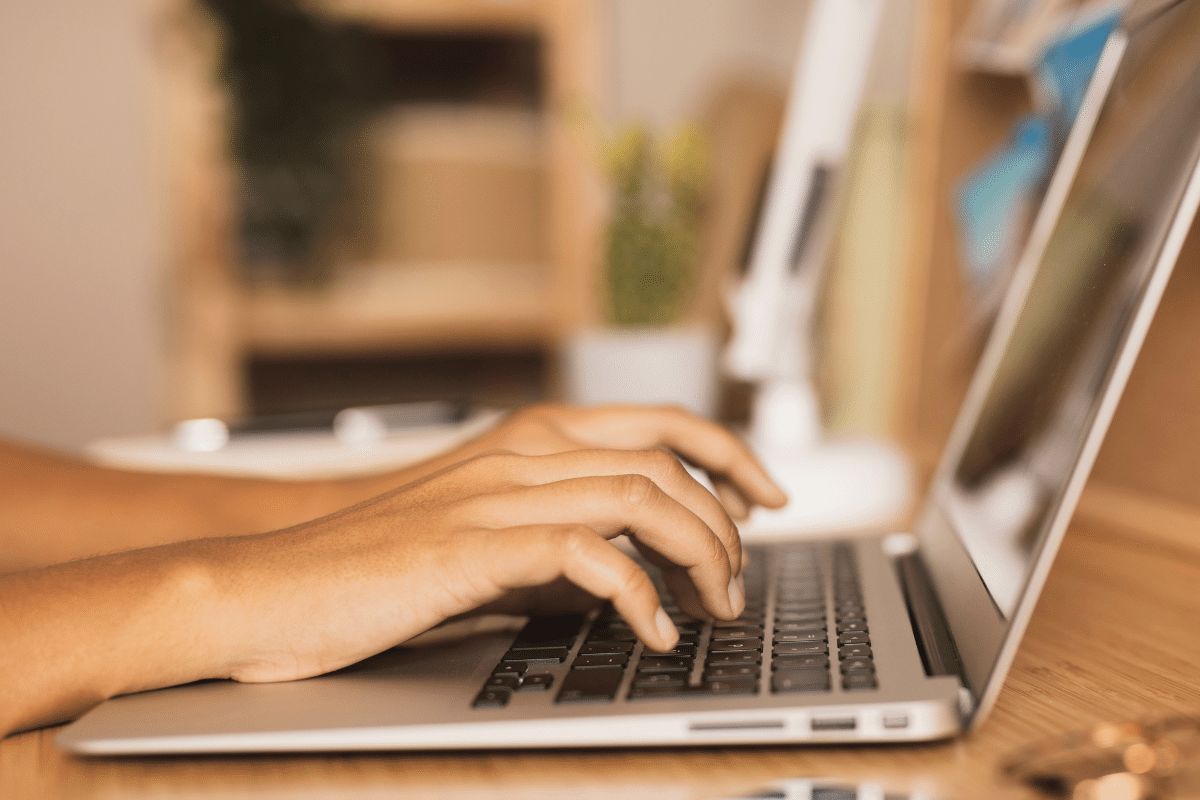 Mãos de pessoa digitando em teclado de notebook sobre mesa de madeira