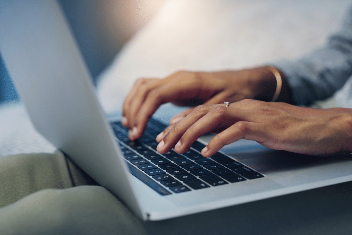 Mãos femininas digitam em teclado de notebook com foco em anel e pulseira dourada