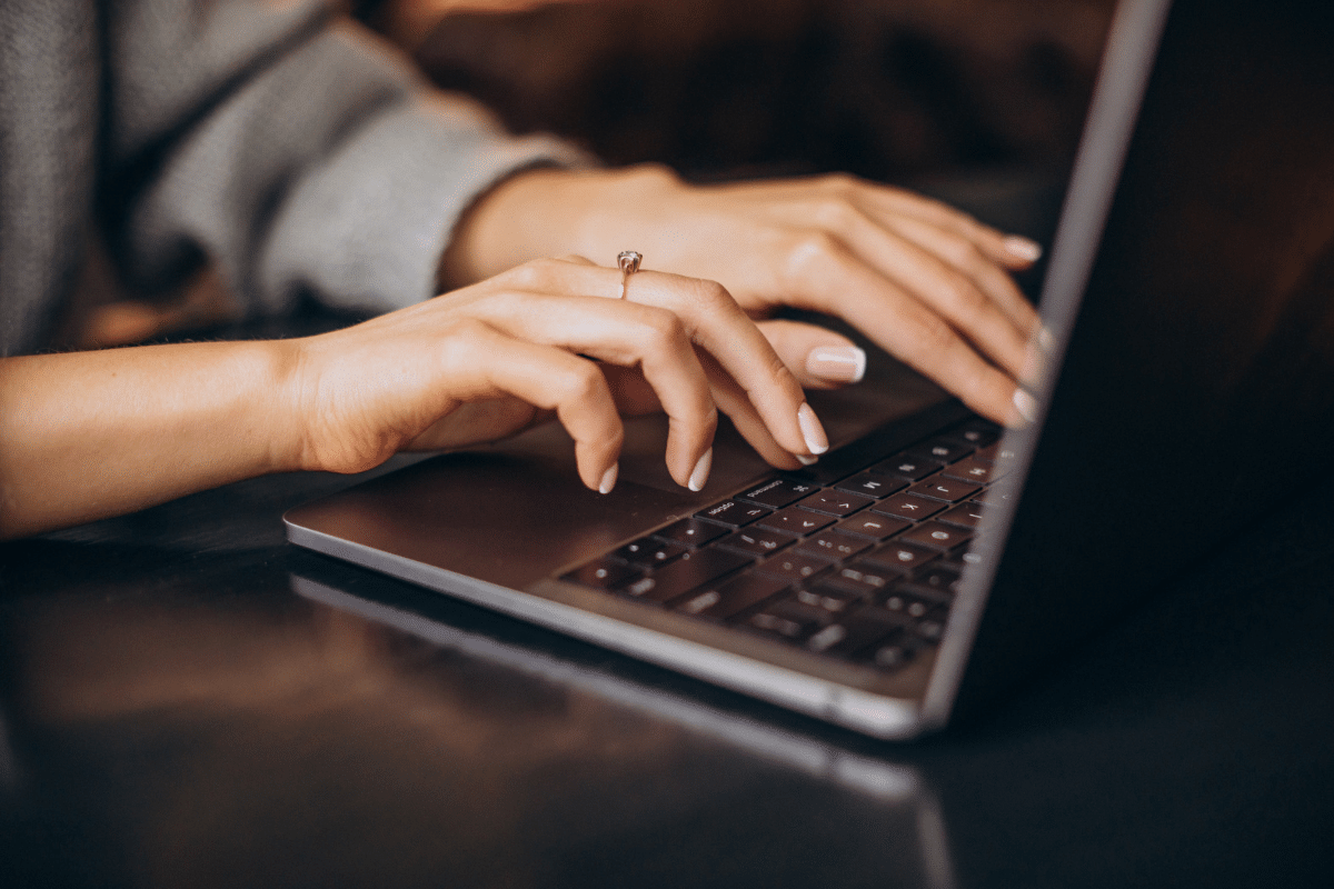Mãos femininas com anel digitando em teclado de notebook sobre mesa escura