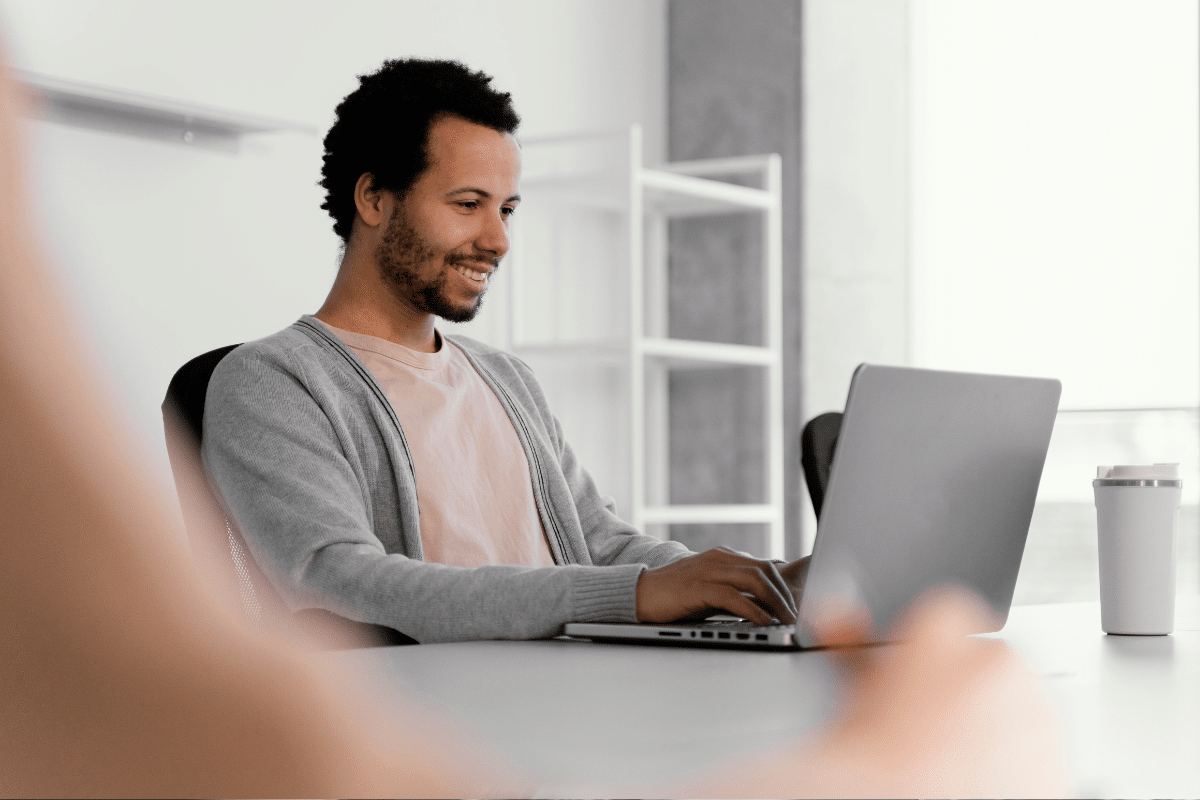 Homem sorridente digitando em notebook enquanto trabalha em mesa de escritório moderno