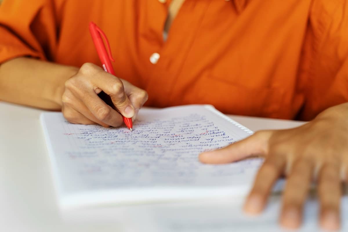Candidato escrevendo em caderno com caneta vermelha representando as inscrições para o processo seletivo da Prefeitura de Patrocínio MG com mais de 130 vagas