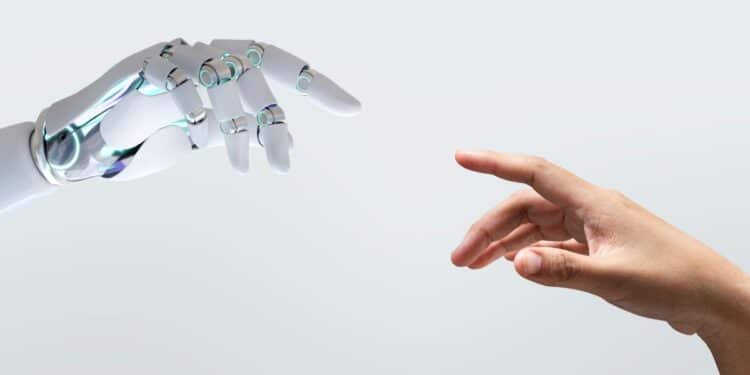 Close em plano médio de uma mão robótica branca e articulada e uma mão humana de pele morena se aproximando, quase se tocando, em um fundo cinza claro neutro. A imagem simboliza a interação entre humanos e inteligência artificial no mercado de trabalho.