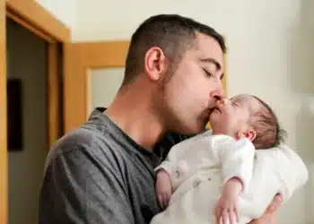 Pai beijando seu recém-nascido em momento de carinho, simbolizando o impacto da ampliação da licença-paternidade.