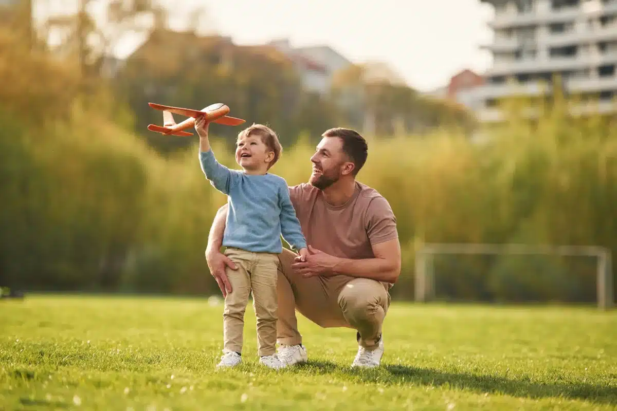 Pai e filho se divertindo no campo com um avião de brinquedo, representando a ampliação da licença-paternidade.