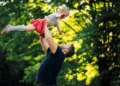 Pai levantando filha no parque, simbolizando o apoio e a importância da licença-paternidade ampliada.