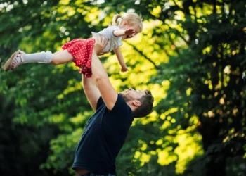 Pai levantando filha no parque, simbolizando o apoio e a importância da licença-paternidade ampliada.