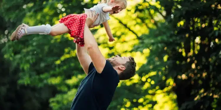 Pai levantando filha no parque, simbolizando o apoio e a importância da licença-paternidade ampliada.