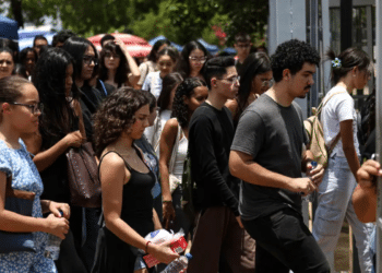 Grupo de jovens segurando garrafas de água, entrando em portão de escola