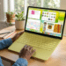 Mulher utiliza notebook amarelo em mesa de madeira com plantas e café ao lado