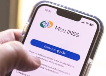 Mão segura celular exibindo tela do aplicativo Meu INSS com botão Entrar com gov.br em destaque